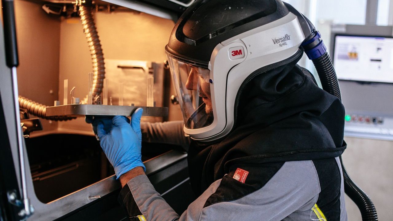 [Translate to Englisch:] Employee removes a printed metal part from the metal 3D printer