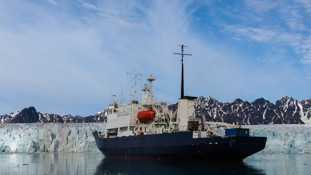 [Translate to Englisch:] Icebreaker on the water in front of ice and mountain landscape