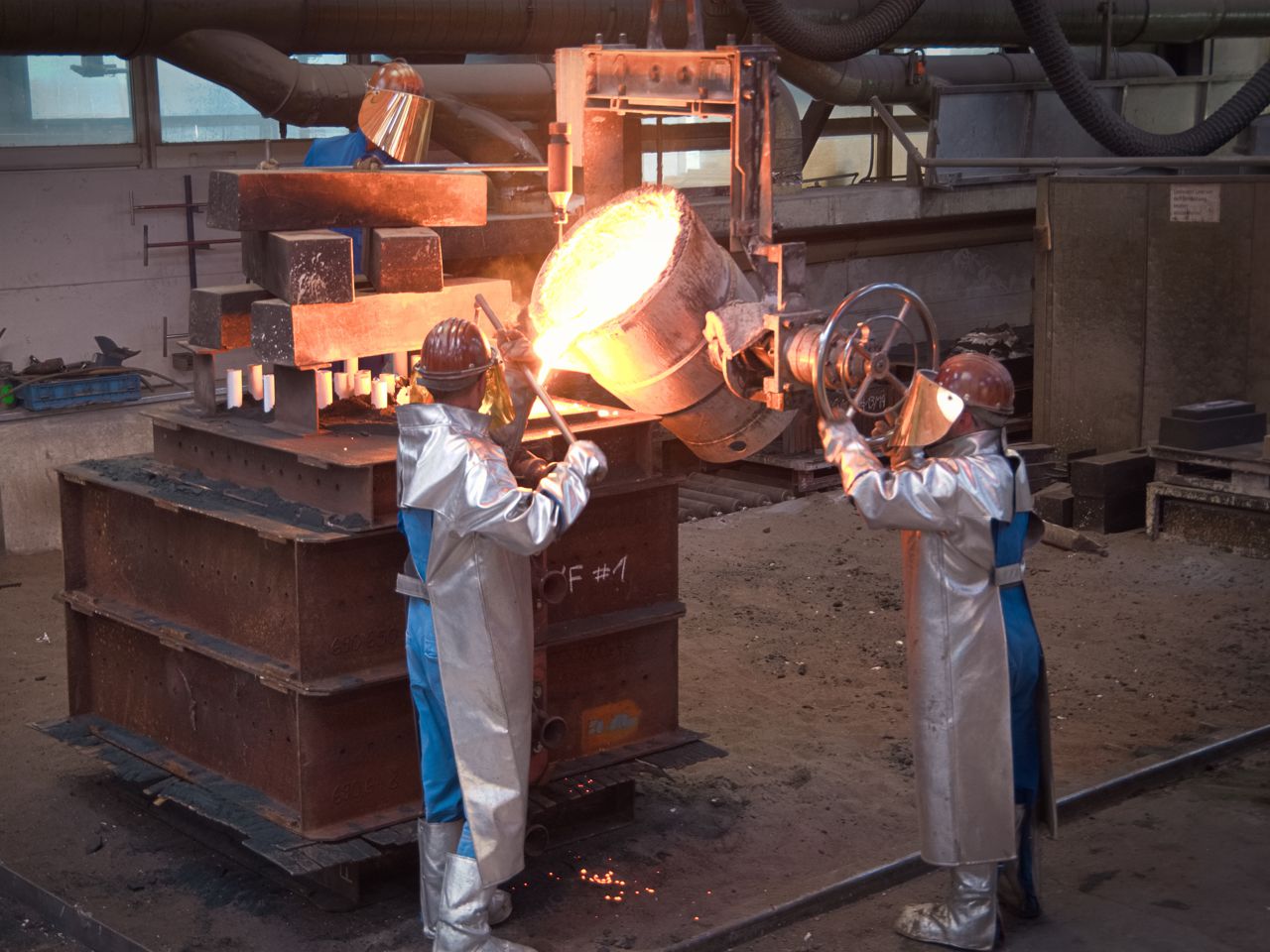 Foundry worker casting steel on particularly large sand mold 
